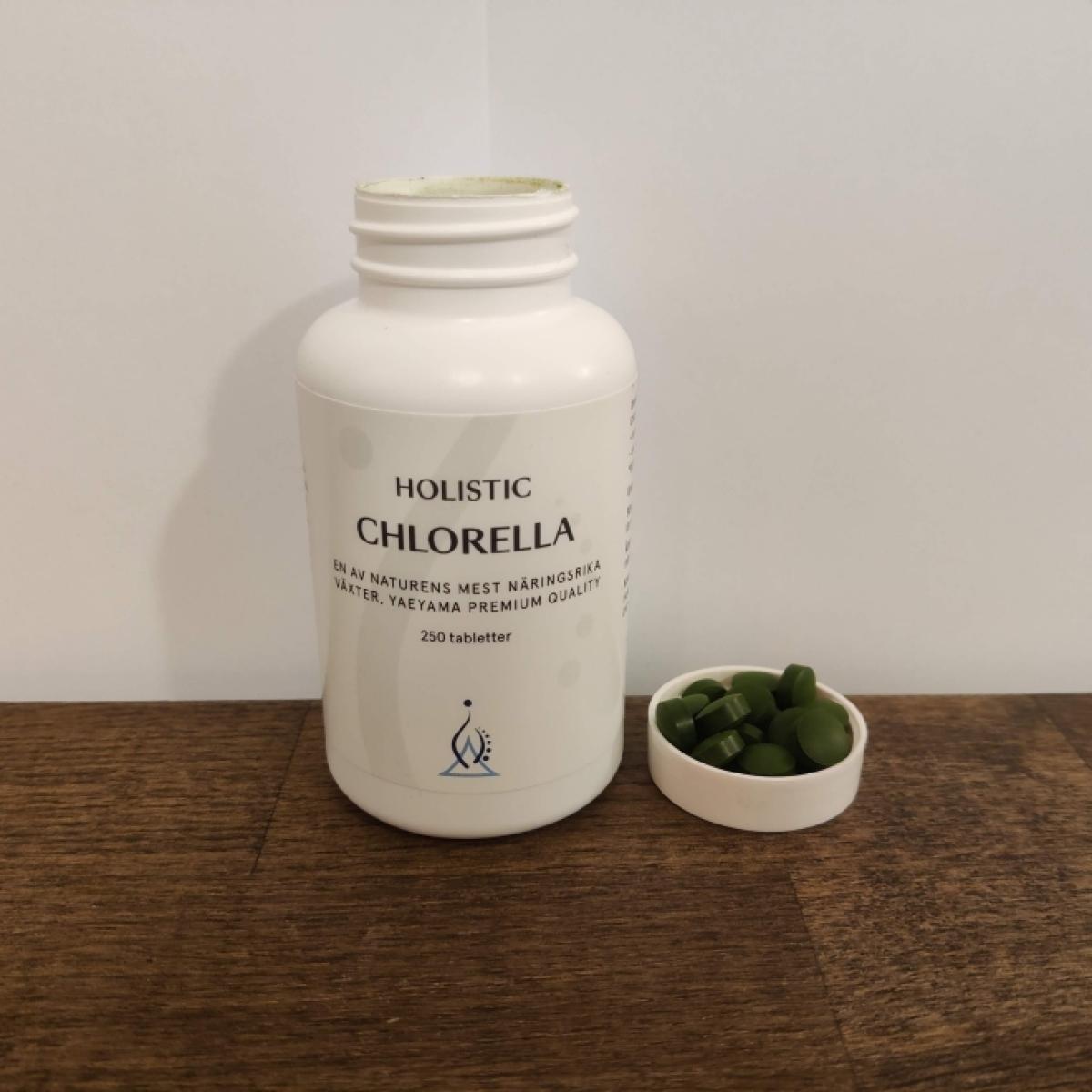 Holistic Chlorella öppnad burk med utspridda tabletter på mörk bänk taget av oss