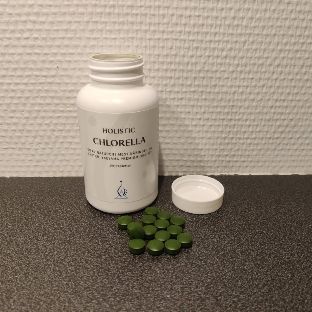 Holistic Chlorella öppnad burk med utspridda tabletter på mörk bänk taget av oss
