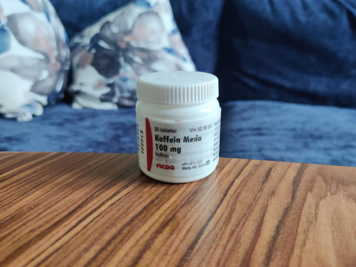 Meda Koffein 100 mg i liten vit burk på soffbordet, foto av oss