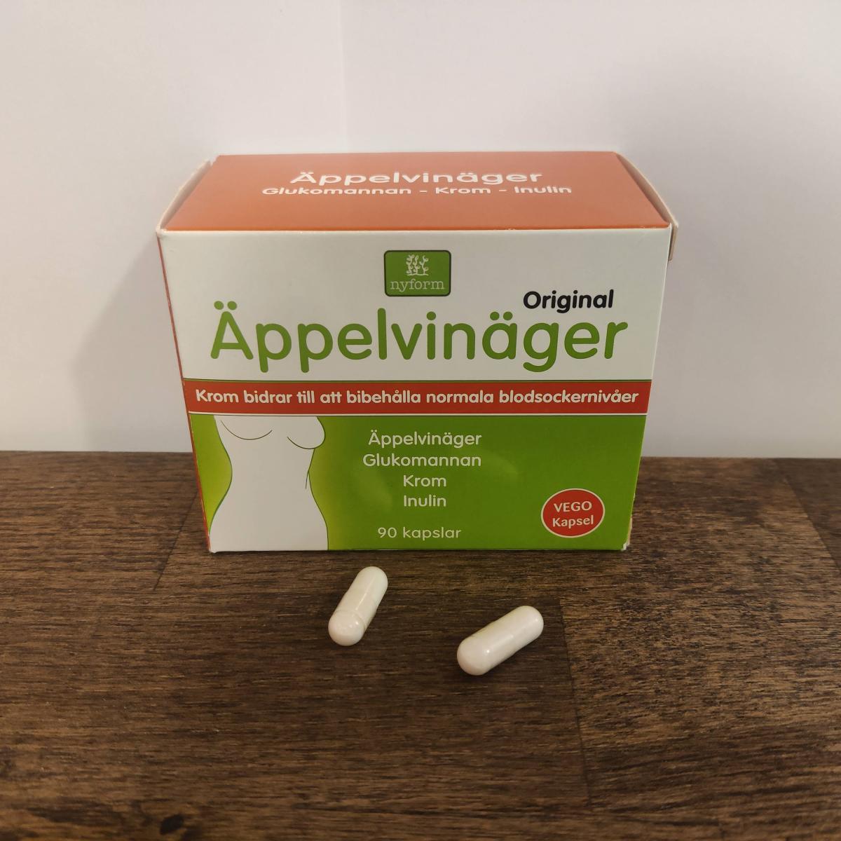 Två kapslar framför förpackningen Nyform Äppelvinäger Krom fotograferat av oss