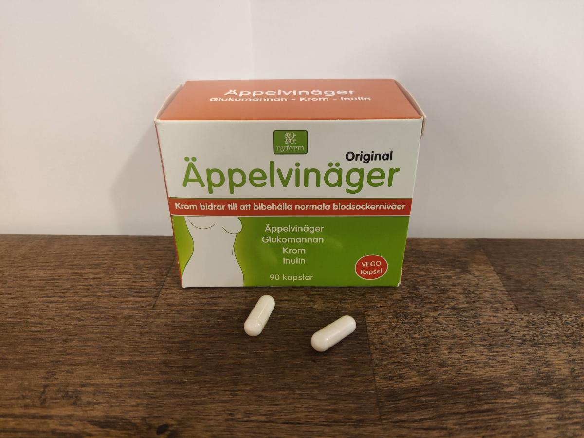 Två kapslar framför förpackningen Nyform Äppelvinäger Krom fotograferat av oss