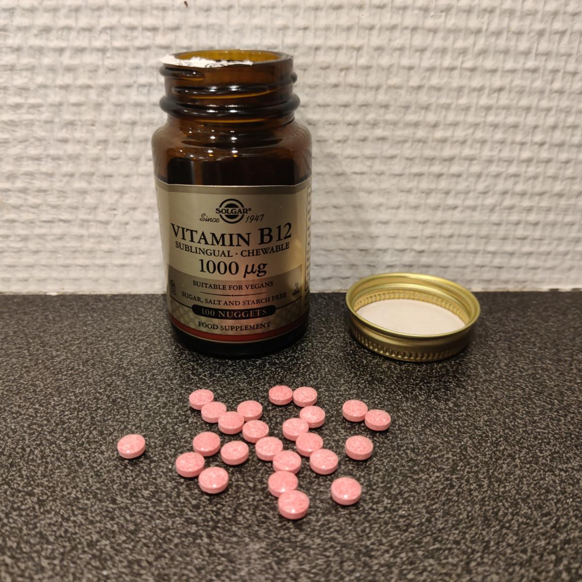 Solgar B12 tuggtabletter öppnad burk och utspridda rosa tabletter foto av oss