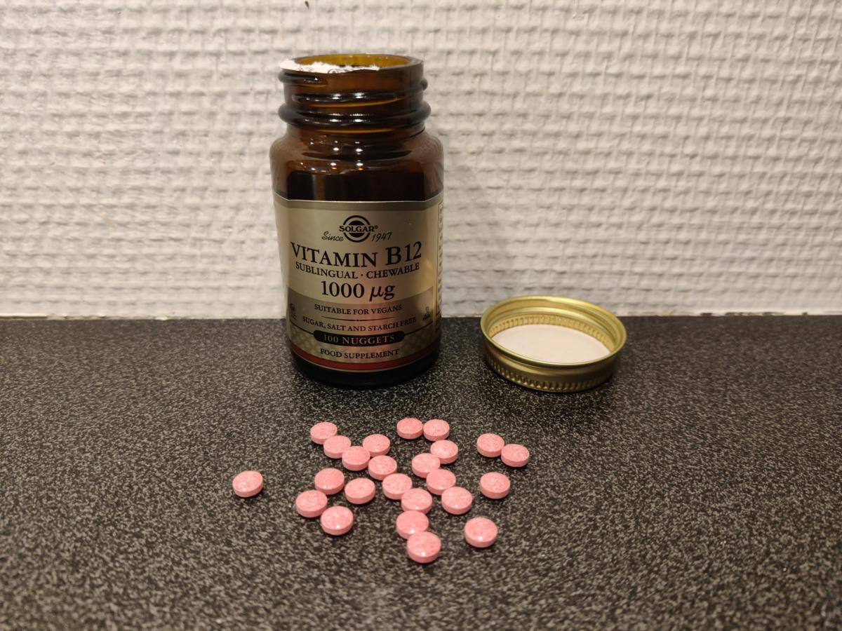 Solgar B12 tuggtabletter öppnad burk och utspridda rosa tabletter foto av oss