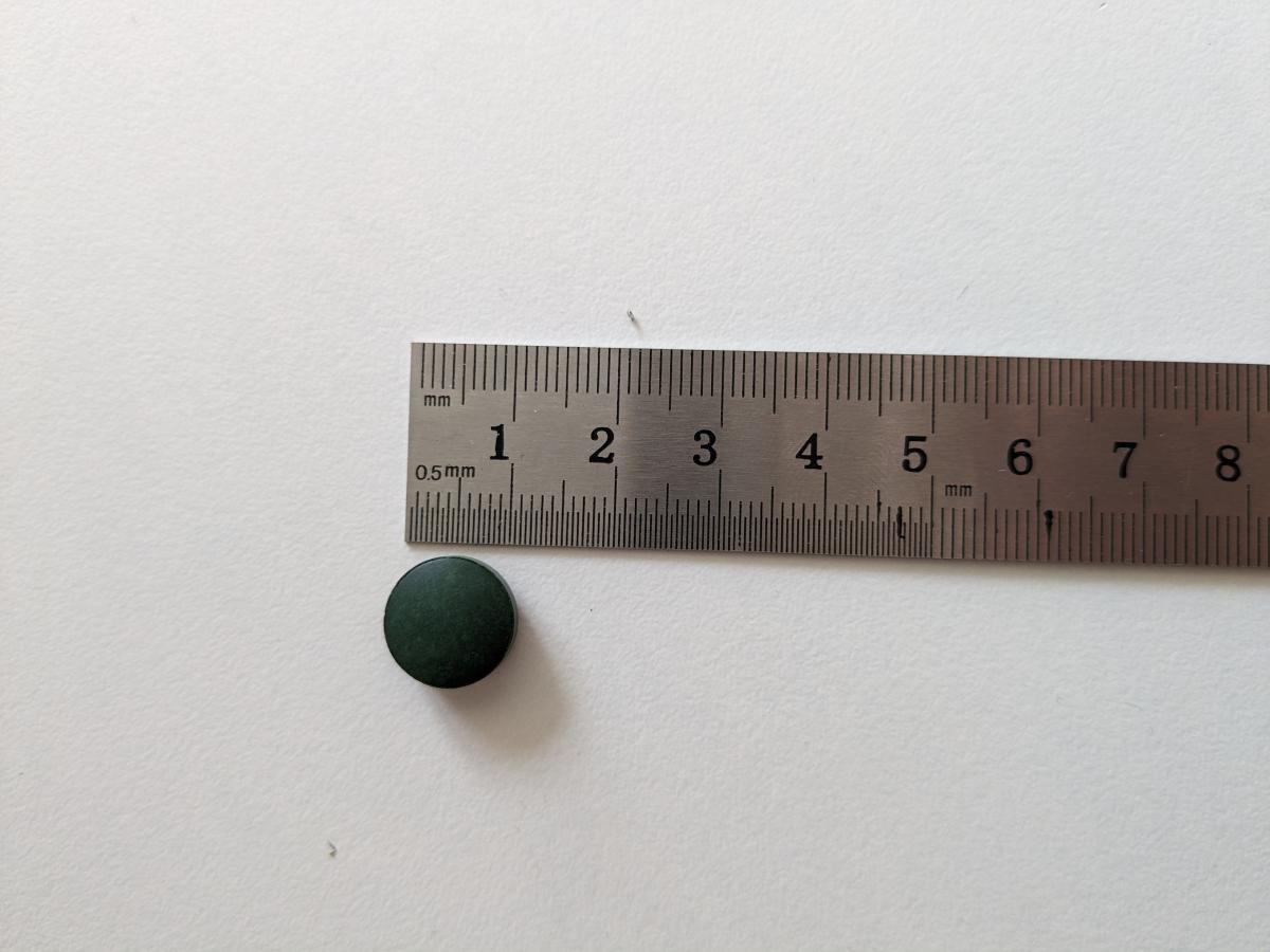 Närbild av spirulinatablett bredvid linjal cirka 11 mm, egen testbild